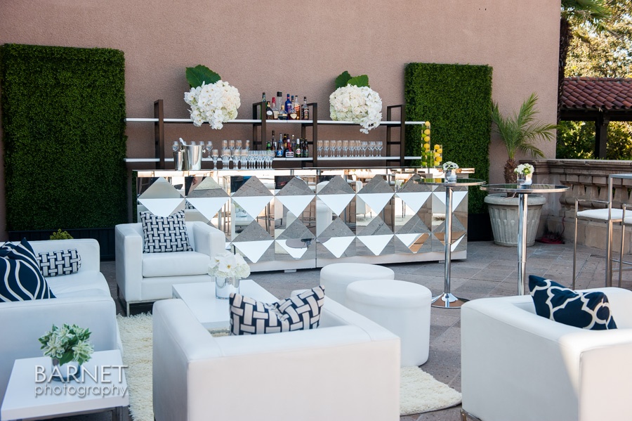Luxury event furniture cost example with white lounge seating, mirrored bar, cocktail tables, and outdoor event décor.