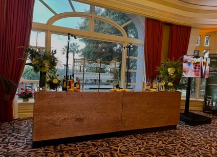 Wood event bar rental setup with floral decor in an elegant indoor reception space